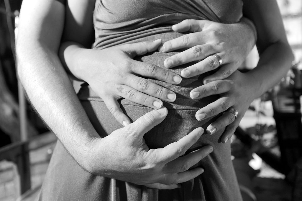 mother and father to be holding the woman's pregnant tummy during the first trimester