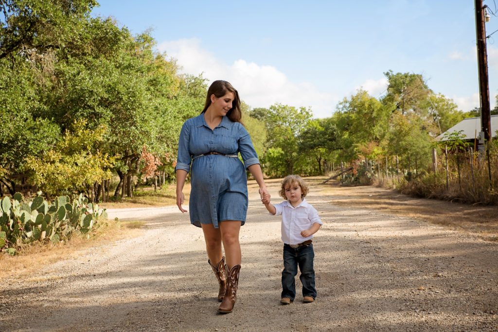 Pregnant woman in denim dress holding hands with her son