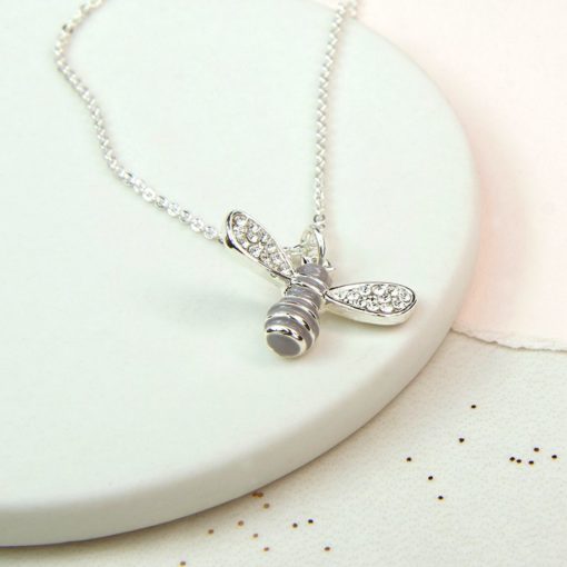 A silver-plated enamel bee necklace with crystal wings on display.