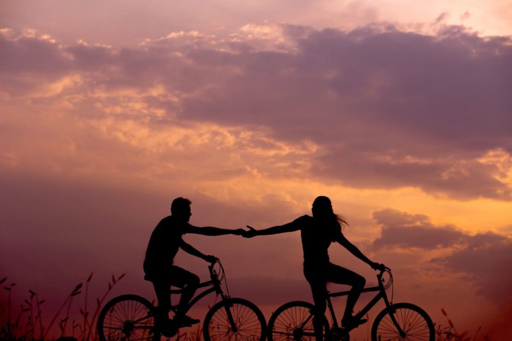 2 cyclists holding hands against a sunset