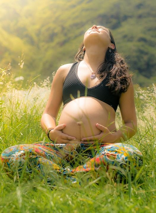 Pregnant woman sitting crossed legged in a field, looking up to the sun